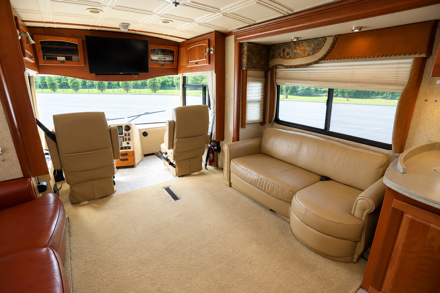 Vectra living area with tan and cognac leather sofas, honey-cherry wood cabinetry and a wall-mounted TV, looking forward to the two front captain's chairs and the one-piece windshield