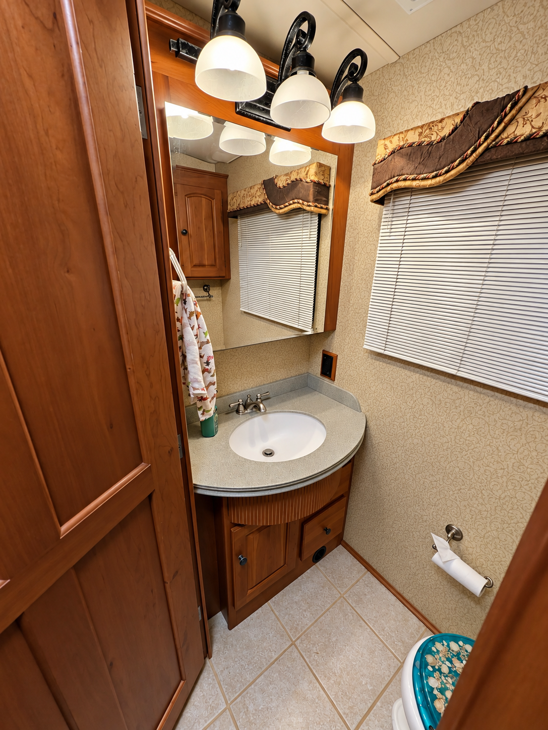 Vectra bathroom vanity — oval sink in a solid-surface counter, warm wood cabinet, framed mirror and window with mini-blinds