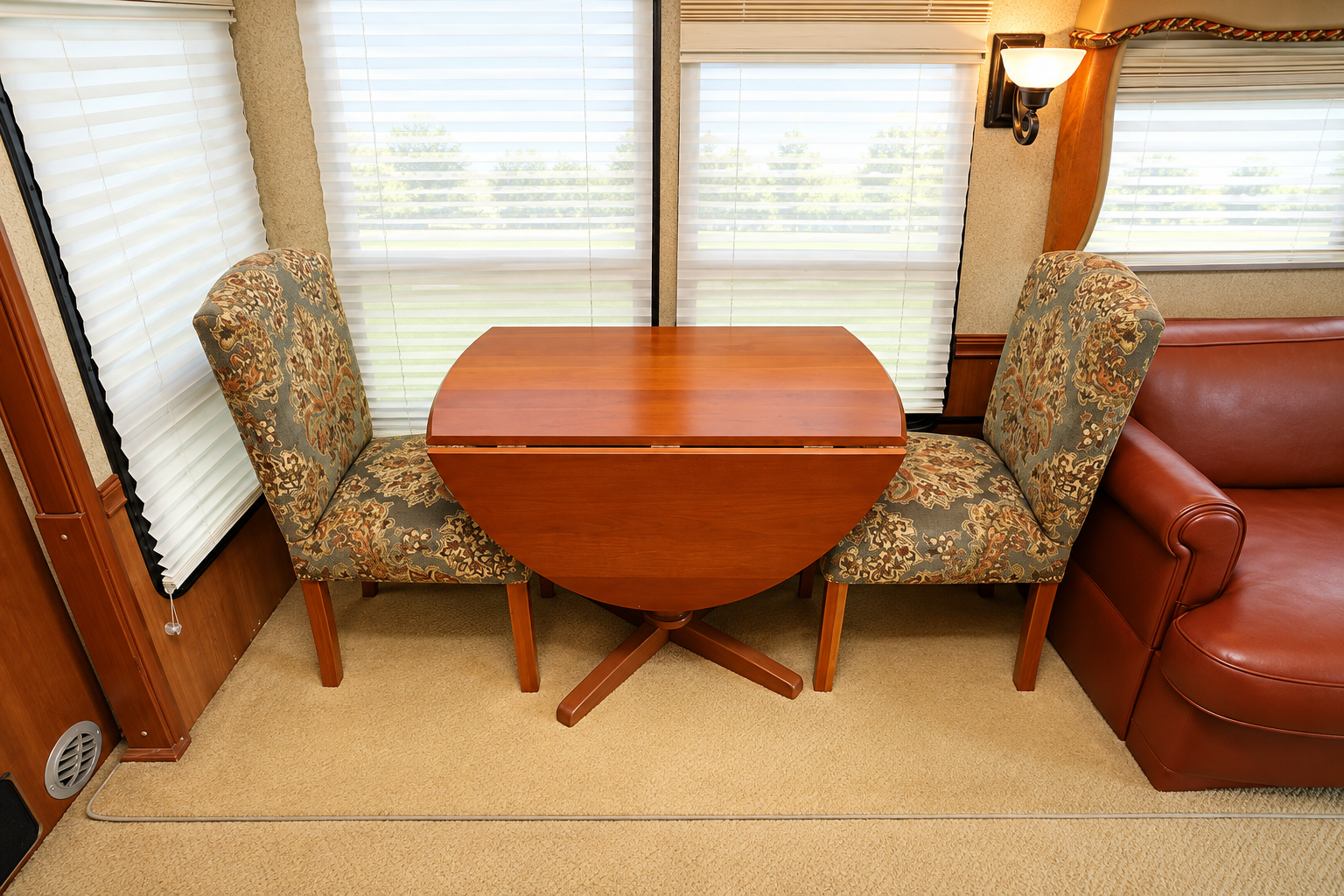 Vectra dinette with a cherry drop-leaf pedestal table and two tapestry-upholstered chairs beneath day-night shades, beside a red leather sofa