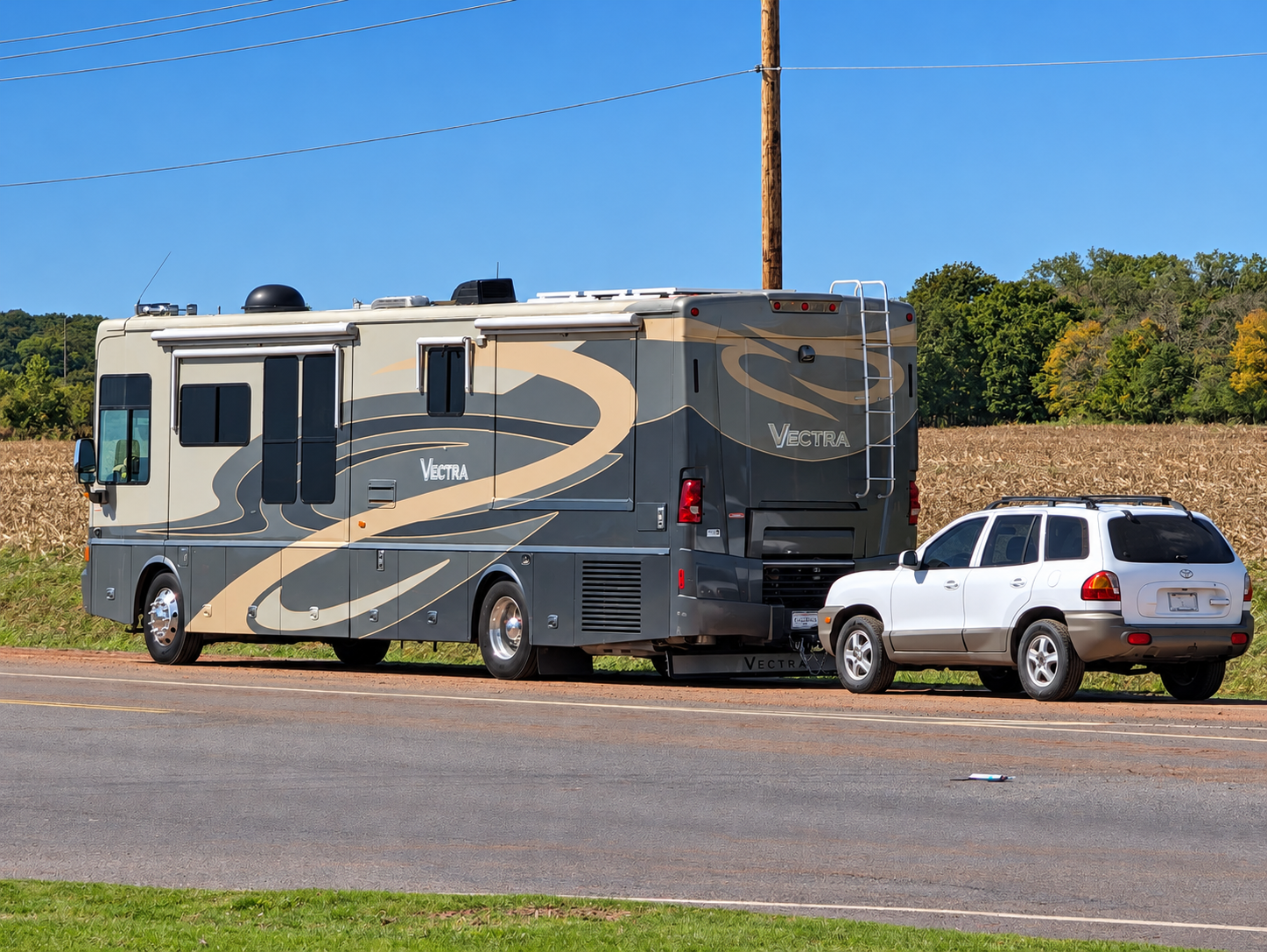 Winnebago Vectra rear three-quarter view flat-towing a white Hyundai Santa Fe beside a harvested field