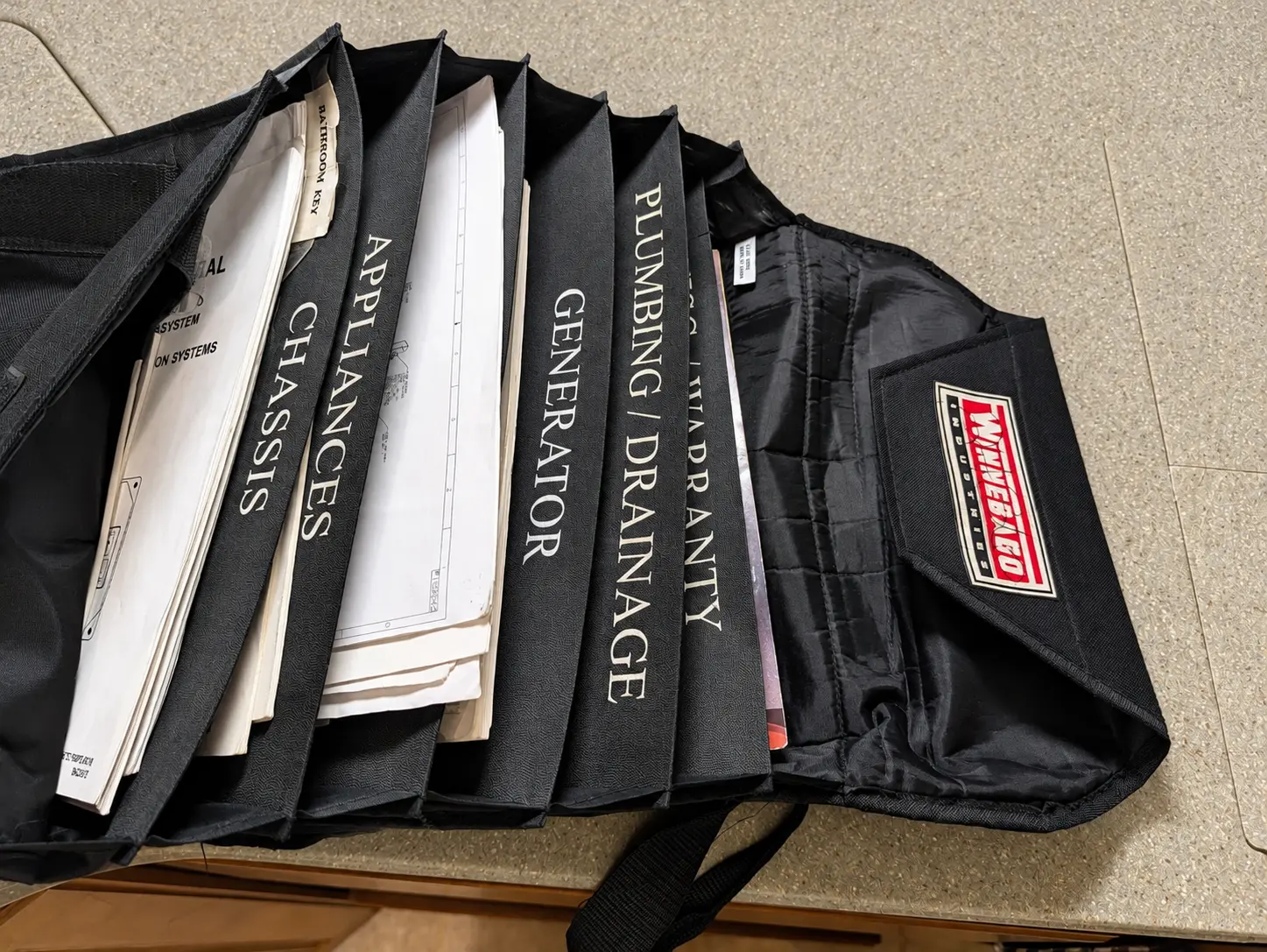 Original Winnebago manuals and owner documentation organized in a black Winnebago Industries accordion case on a countertop